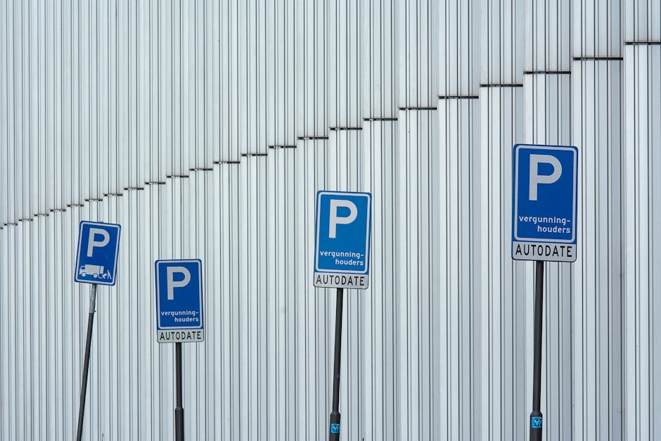 A blue parking sign with a white wheelchair symbol indicating accessible parking is positioned on a yellow pole on a street. In the background, there are several parked cars, including a dark red vehi